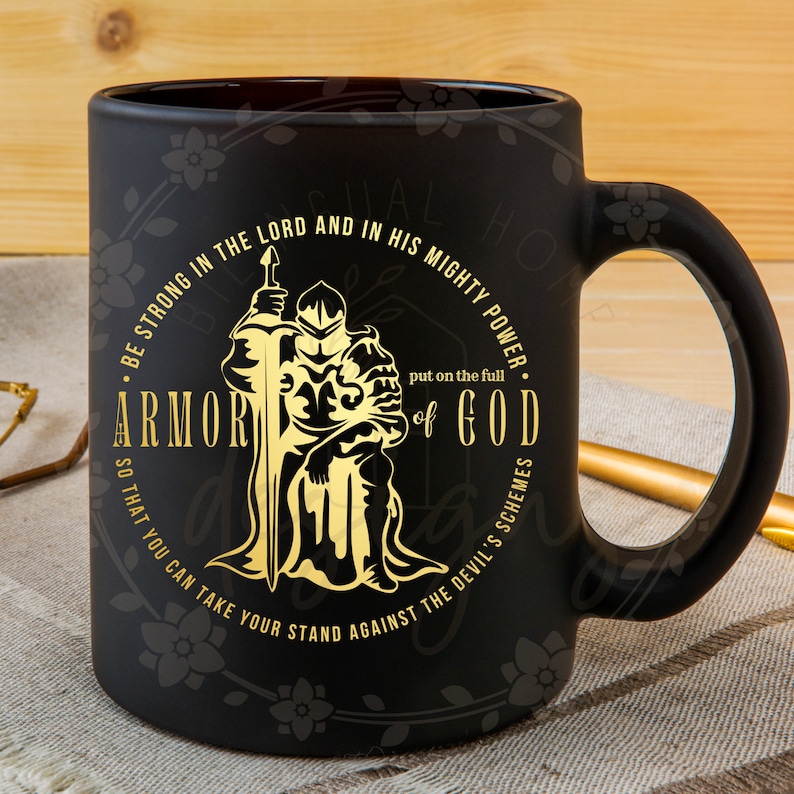 Puede incluir: Taza de cer&aacute;mica negra con un dise&ntilde;o dorado de un caballero con armadura sosteniendo una espada. El texto alrededor del caballero dice "Sean fuertes en el Se&ntilde;or y en su poder. P&oacute;nganse la armadura completa de Dios para que puedan resistir los planes del diablo."