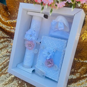 May include: A white gift box with a blue and white lace design. The box contains a white candle with lace and flowers, a white heart-shaped box with a blue ribbon, and a blue and white lace box with flowers.
