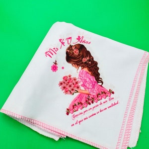 May include: White fabric with pink trim and a printed image of a girl with brown hair and a pink dress holding a bouquet of pink flowers. The text "Mis 2o Años" is printed in pink at the top of the fabric. The text "Gracias por ser parte de este Dia en el que mis sueños se hacen realidad." is printed in black at the bottom of the fabric.