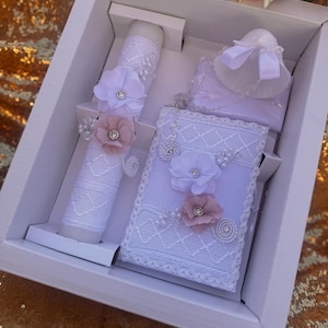 May include: White gift box with a white candle, a white lace-trimmed box, and a white lace-trimmed hat with a white ribbon. The candle and box are decorated with white and pink flowers.