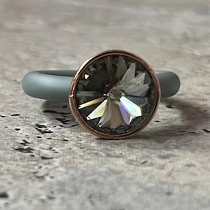 Könnte beinhalten: Ein grauer Silikonring mit einer Roségoldfassung und einem klaren Kristallstein.