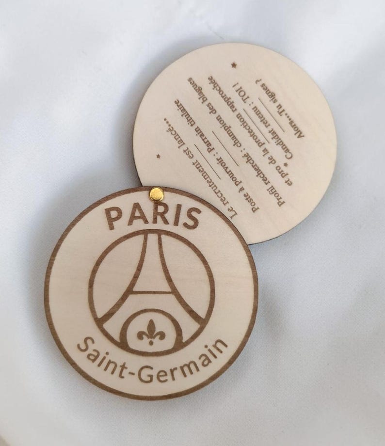 Puede incluir: Dos posavasos redondos de madera. Uno presenta el logotipo del Paris Saint-Germain, con la Torre Eiffel y la flor de lis, y las palabras "Paris" y "Saint-Germain". El segundo posavasos tiene texto en franc&eacute;s.