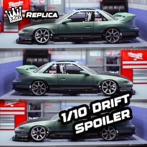 May include: A green 1/10 scale drift car replica with a black spoiler and black wheels. The car has a black and white sticker on the side that says "Replica". The car is sitting on a gray surface.