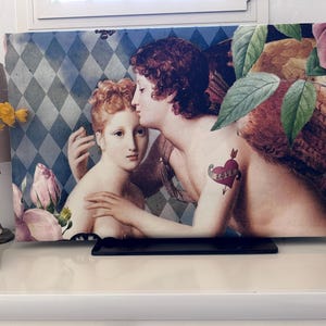 Könnte beinhalten: Ein rechteckiger Kunstdruck mit einer Renaissance-Szene von zwei sich umarmenden Figuren. Eine Figur hat ein Herz-Tattoo mit dem Wort "LOVE". Der Hintergrund hat ein blau-weißes Rautenmuster mit floralen Akzenten.