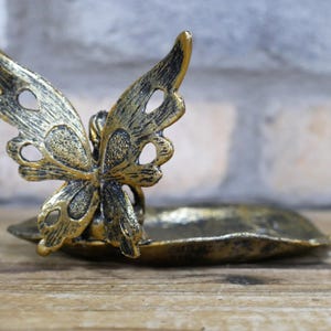 May include: A gold metal butterfly trinket dish with a leaf-shaped base. The butterfly has intricate details and a distressed finish.