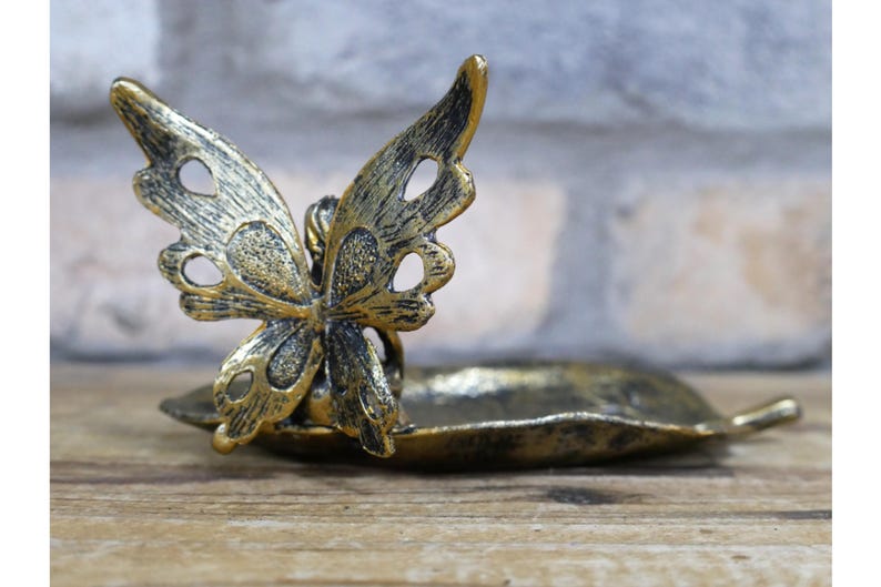 May include: A gold metal butterfly trinket dish with a leaf-shaped base. The butterfly has intricate details and a distressed finish.