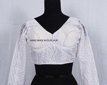 Puede incluir: Blusa blanca bordada con mangas largas y cuello en V. La blusa tiene un delicado patrón floral y el texto "HAND MADE BLOUSE HUB" es visible en la parte delantera.