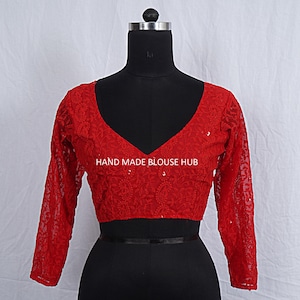 Puede incluir: Blusa roja bordada con mangas largas y cuello en V. La blusa está hecha de una tela transparente y tiene un delicado patrón floral. El texto "HAND MADE BLOUSE HUB" es visible en la parte delantera de la blusa.