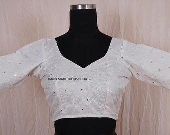 May include: White cotton blouse with short sleeves and a V-neckline. The blouse is decorated with small, round, mirrored embellishments. The text "HAND MADE BLOUSE HUB" is printed on the front of the blouse.