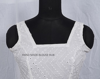 May include: White, square-neck blouse with embroidered details. The blouse features a geometric pattern and eyelet cutouts. The text "HAND MADE BLOUSE HUB" is printed on the front. The blouse is displayed on a black mannequin.