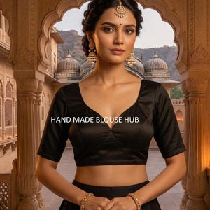 May include: A black, short-sleeved blouse with a V-neck. The blouse is made of a smooth fabric and is worn with a matching skirt. The text "HAND MADE BLOUSE HUB" is visible on the blouse.