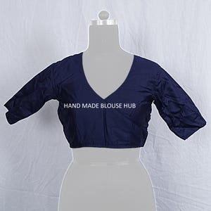 Pode incluir: Uma blusa azul marinho com decote em V profundo e mangas três quartos. A blusa é exibida em um manequim e apresenta o texto "HAND MADE BLOUSE HUB". O tecido parece ter um leve brilho.
