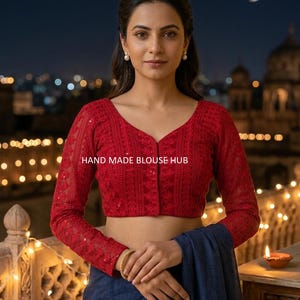 Peut inclure: Un chemisier rouge à manches longues avec une broderie complexe et un décolleté en V. Le chemisier a une fermeture à boutons et est associé à un vêtement bleu. Le texte "HAND MADE BLOUSE HUB" est visible. L'arrière-plan présente une scène de nuit.