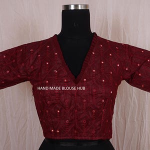 Puede incluir: Una blusa bordada de color granate con escote en V y mangas cortas. La blusa está decorada con pequeñas lentejuelas redondas y tiene una etiqueta que dice "HAND MADE BLOUSE HUB".