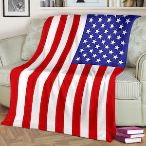 May include: A red, white, and blue American flag throw blanket. The blanket is folded and draped over a white couch.