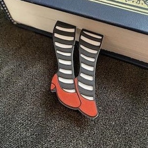 May include: A red and black striped bookmark with red shoes, shaped like a pair of legs sticking out from a book.