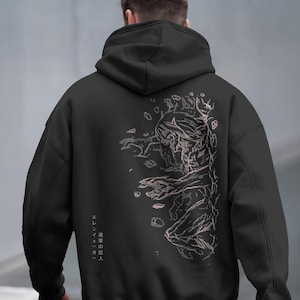 May include: Black hoodie featuring a detailed pink and white illustration of a Titan from the anime series. The design includes the text "Eren Yeager" in Japanese characters. The hoodie has a drawstring hood and a kangaroo pocket.