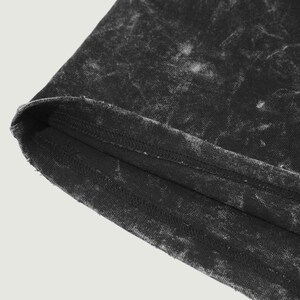 May include: Close-up of the bottom edge of a black t-shirt with a faded, distressed look. The fabric has a subtle white pattern.