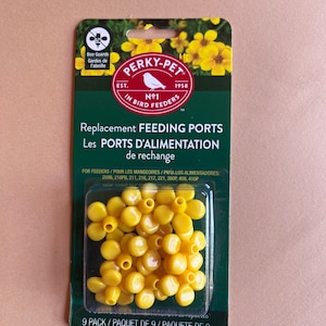 May include: A package of Perky-Pet replacement feeding ports. The package is green with yellow flowers and the Perky-Pet logo. The package contains a clear plastic tray filled with yellow, flower-shaped feeding ports. The text on the package reads "Replacement Feeding Ports".