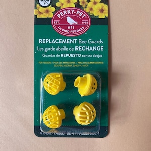 May include: A package of four yellow replacement bee guards for bird feeders. The package has the Perky-Pet logo and text that reads "REPLACEMENT Bee Guards". The package is green with yellow flowers at the top.