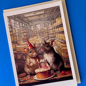 May include: Two mice wearing party hats celebrate with a birthday cake in a cheese factory. The cake has lit candles and is on a plate with a red cherry on top. The mice are in a large room with shelves of cheese wheels.