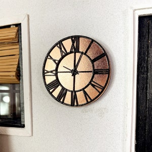Könnte beinhalten: Eine schwarze und kupferfarbene Uhr mit römischen Ziffern an einer weißen Wand.