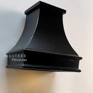 Puede incluir: Una campana extractora en miniatura negra con un diseño curvo, colocada sobre una estufa en miniatura. La estufa tiene un cuerpo blanco, una encimera negra y perillas doradas. El texto "MUSTARD Miniatures" es visible.