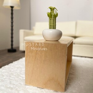 May include: Miniature wooden coffee table with a white ceramic pot holding a green bamboo plant. The table is light brown and has a simple, open design. The text "MUSTARD Miniatures" is visible on the table.