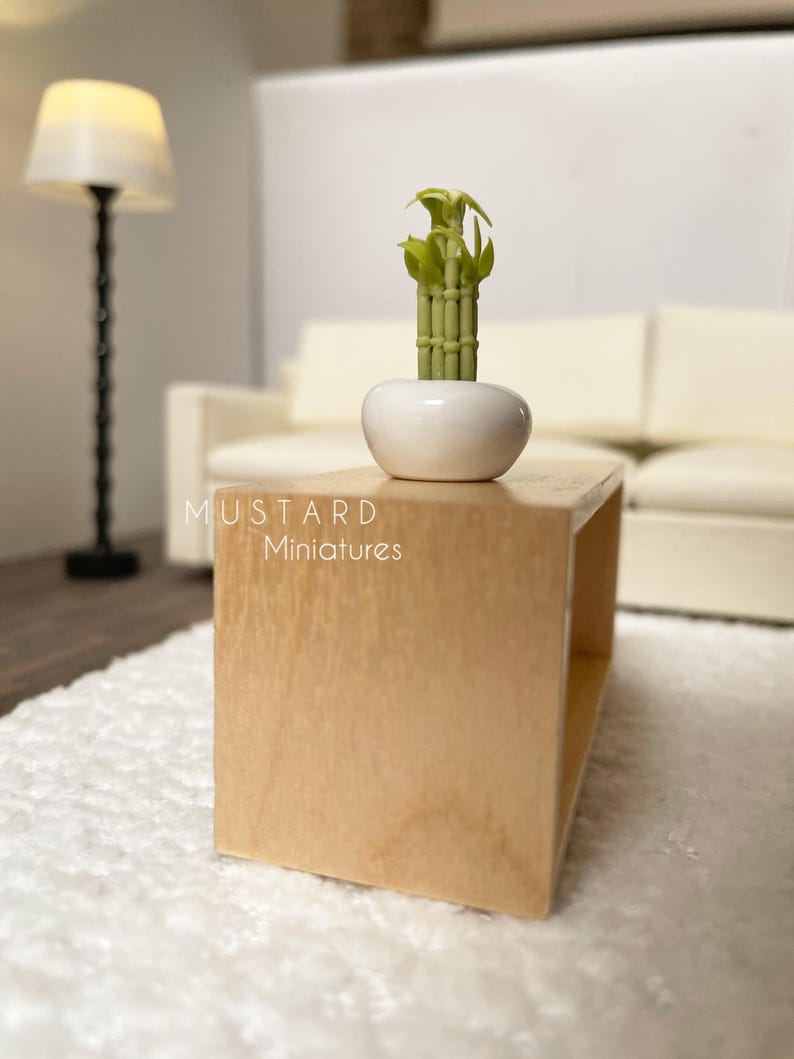 May include: Miniature wooden coffee table with a white ceramic pot holding a green bamboo plant. The table is light brown and has a simple, open design. The text "MUSTARD Miniatures" is visible on the table.