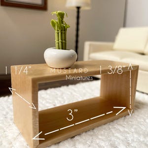 May include: A miniature wooden coffee table with a rectangular design, measuring 3 inches long, 1 1/4 inches wide, and 3/8 inches high. It features a small white ceramic pot with a green bamboo plant. The text "MUSTARD Miniatures" is visible.