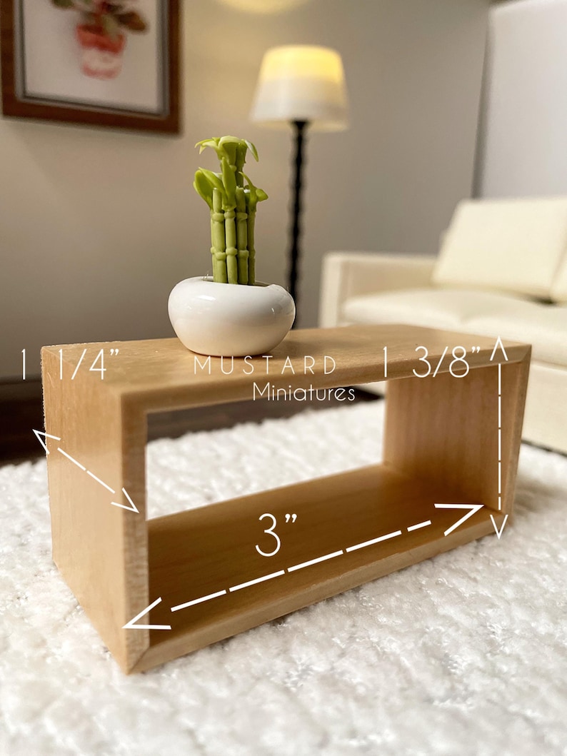 May include: A miniature wooden coffee table with a rectangular design, measuring 3 inches long, 1 1/4 inches wide, and 3/8 inches high. It features a small white ceramic pot with a green bamboo plant. The text "MUSTARD Miniatures" is visible.