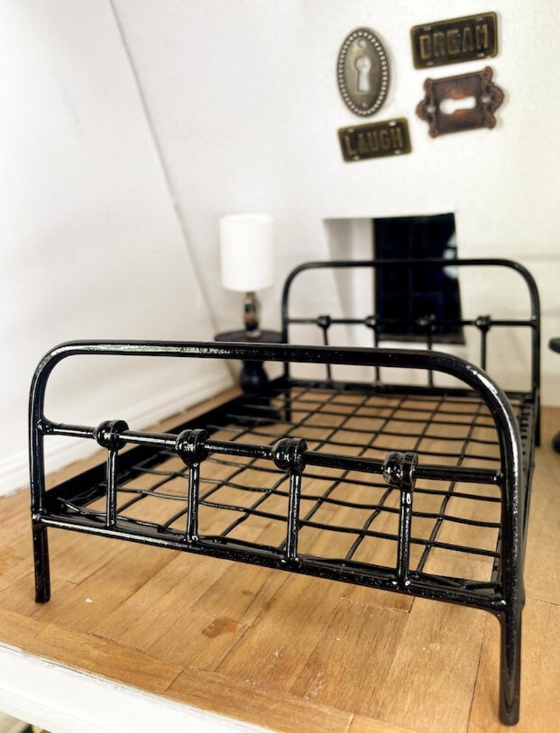 May include: Black metal bed frame with a wire mesh mattress. The bed frame has rounded knobs on the top and bottom of the frame. The bed is sitting on a wooden floor.