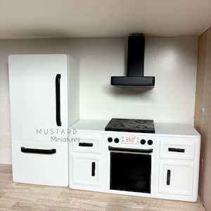Puede incluir: Un juego de cocina en miniatura blanco que incluye un refrigerador con manijas negras, una campana extractora negra y una estufa con placa y puerta de horno negras. El panel de control muestra 350 grados. Se lee el texto MUSTARD Miniatures.