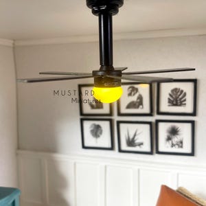 Puede incluir: Ventilador de techo negro en miniatura con seis aspas y luz amarilla. El ventilador est&aacute; montado en un techo blanco. El texto "MUSTARD Miniatures" es visible. Seis grabados bot&aacute;nicos enmarcados cuelgan de la pared.
