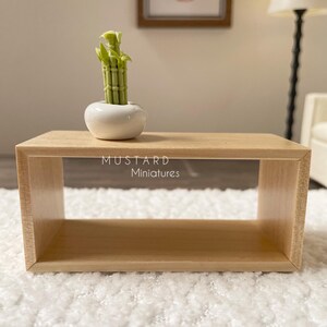 May include: A miniature wooden coffee table with a small white ceramic pot holding a green bamboo plant. The table has a rectangular shape and is made of light-colored wood. The text "MUSTARD Miniatures" is visible.