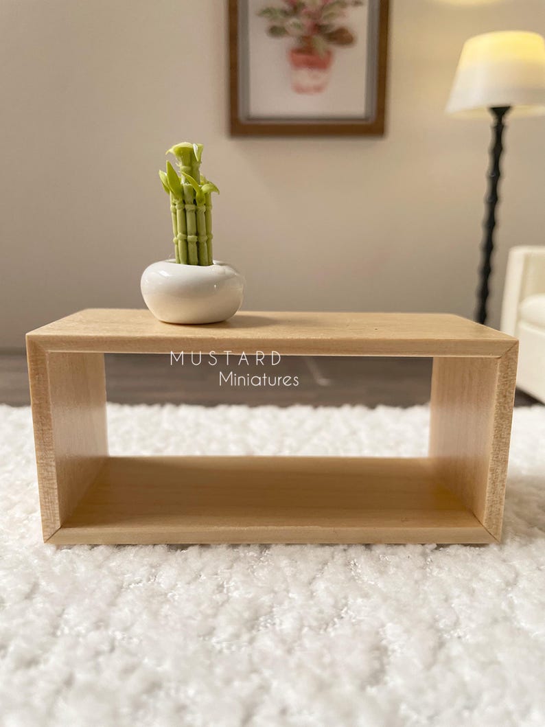 May include: A miniature wooden coffee table with a small white ceramic pot holding a green bamboo plant. The table has a rectangular shape and is made of light-colored wood. The text "MUSTARD Miniatures" is visible.