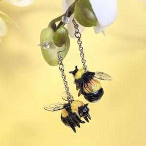 Könnte beinhalten: Ein Paar Ohrringe mit silbernen Ketten und einem schwarzen und gelben Hummel-Anhänger an jedem Ohrring.