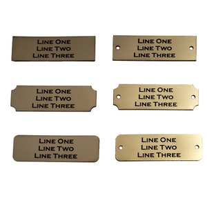 May include: Six gold-colored metal nameplates with rounded corners and holes for hanging. Each plate has three lines of text: "LINE ONE", "LINE TWO", and "LINE THREE".