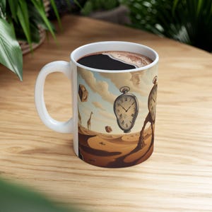 Peut inclure: Un mug en céramique blanche orné d'une illustration de paysage désertique surréaliste avec des montres de poche fondantes, des cubes géométriques flottants et des girafes au loin sous un ciel nuageux. L'intérieur contient du café noir.