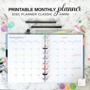 Op de afbeelding: Open maandplanner met kleurrijke schijfbinding, pastelkleurige vakjes voor elke dag en de tekst "Monthly planner". De afbeelding bevat potloden, washitape en decoratieve paperclips. De tekst "Printable Monthly Planner" staat bovenaan.