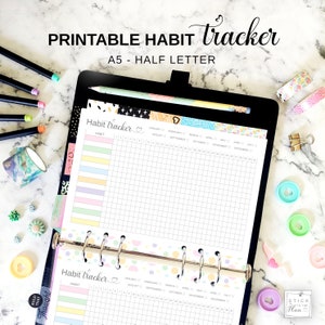 May include: A black binder with two printable habit tracker pages. The pages are white with a grid pattern and colorful headers. The pages are labeled "Habit tracker" and include months of the year. The binder is labeled "A5 - Half Letter".