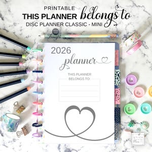 May include: A 2026 disc-bound planner with a white cover featuring a grey heart graphic and the text "THIS PLANNER BELONGS TO". The planner is surrounded by colourful pens, patterned washi tape, small metal binder clips, and loose plastic discs.