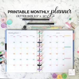 May include: A printable monthly planner with the text "PRINTABLE MONTHLY planner LETTER SIZE 8,5" x 11"" is open to a blank calendar page. The planner is open to a blank calendar page with pastel color accents. Pens, washi tape, and other stationery items are scattered around the planner.