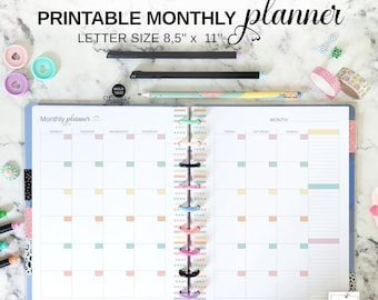 May include: A printable monthly planner with the text "PRINTABLE MONTHLY planner LETTER SIZE 8,5" x 11"" is open to a blank calendar page. The planner is open to a blank calendar page with pastel colour accents. Pens, washi tape, and other stationery items are scattered around the planner.