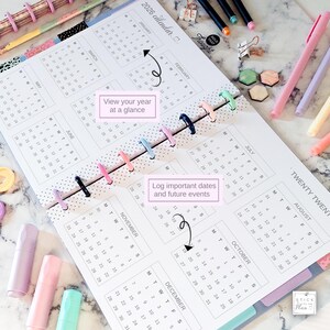 May include: A 2026 disc-bound calendar planner featuring a white page with black text, monthly grids, and colorful plastic binding discs. The page includes the text View your year at a glance and Log important dates and future events with arrows.