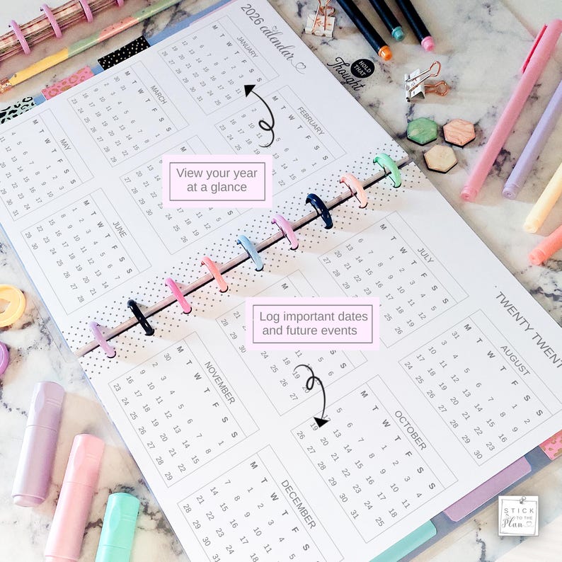 May include: A 2026 disc-bound calendar planner featuring a white page with black text, monthly grids, and colorful plastic binding discs. The page includes the text View your year at a glance and Log important dates and future events with arrows.