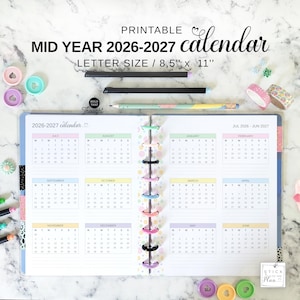 Puede incluir: Calendario imprimible de mitad de año 2026-2027, tamaño carta (21,6 cm x 27,9 cm). El calendario está abierto, mostrando diseños mensuales con pestañas de colores pastel. Incluye lápices, cinta washi y clips decorativos.