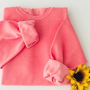 May include: A pink crew neck sweatshirt with long sleeves. The sweatshirt is folded in half and the sleeves are rolled up.