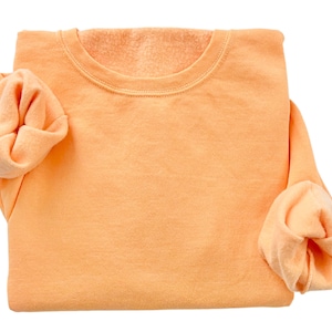 May include: A folded peach-colored sweatshirt with long sleeves.