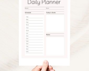 Puede incluir: Un planificador diario imprimible con secciones para el horario, los objetivos del día y las notas. El planificador tiene un fondo rosa claro y texto negro.